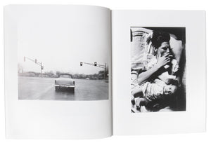 Image of the inside of the photograph book from Larry Clark's "Kiss the Past Hello" set. Image on the left page is of a car at a stop light, image on the right is of a man laying in bed smoking a cigarette with a baby laying on his stomach.